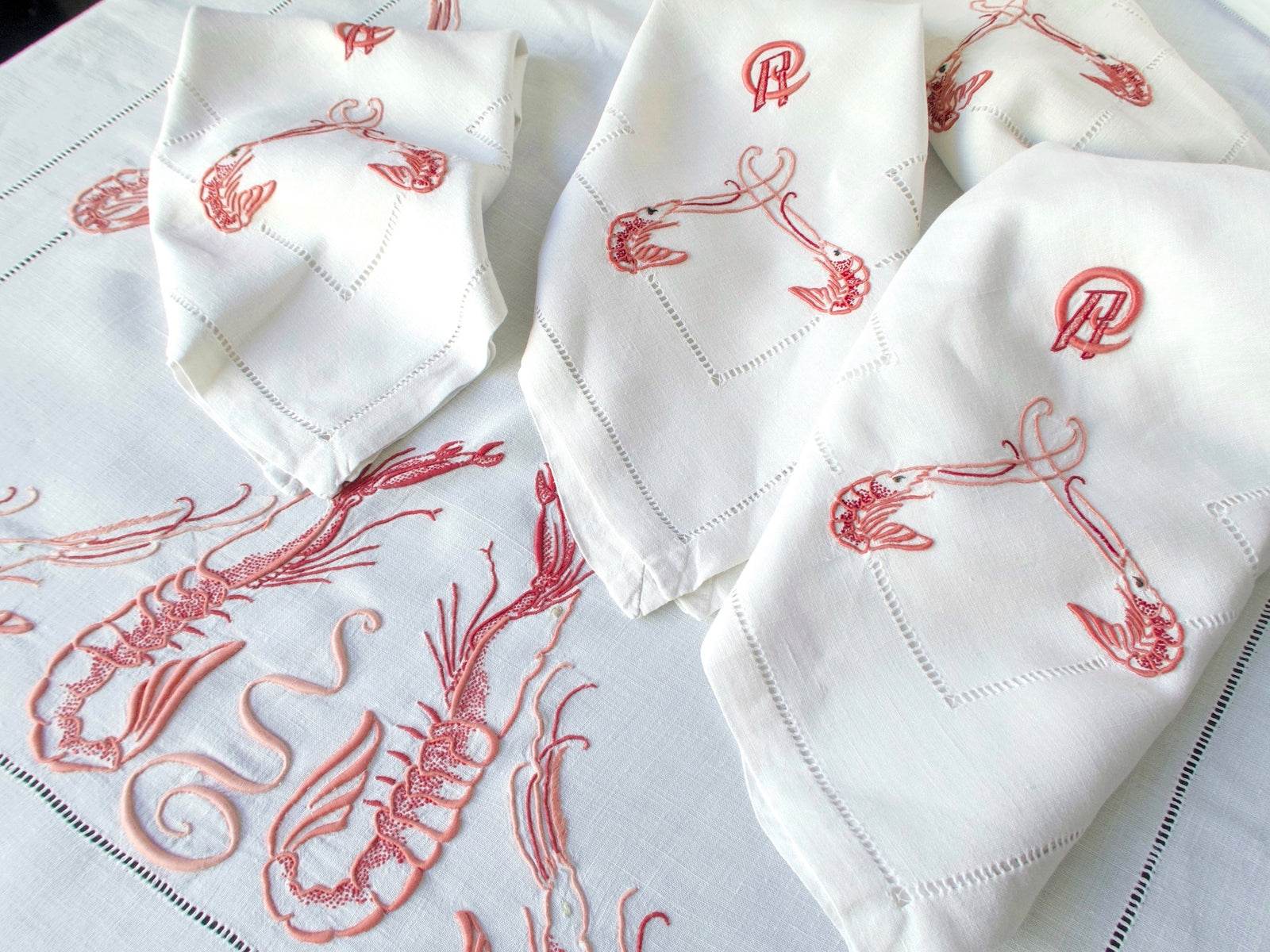 Multiple hand embroidered langoustines across antique French linen tablecloth surface