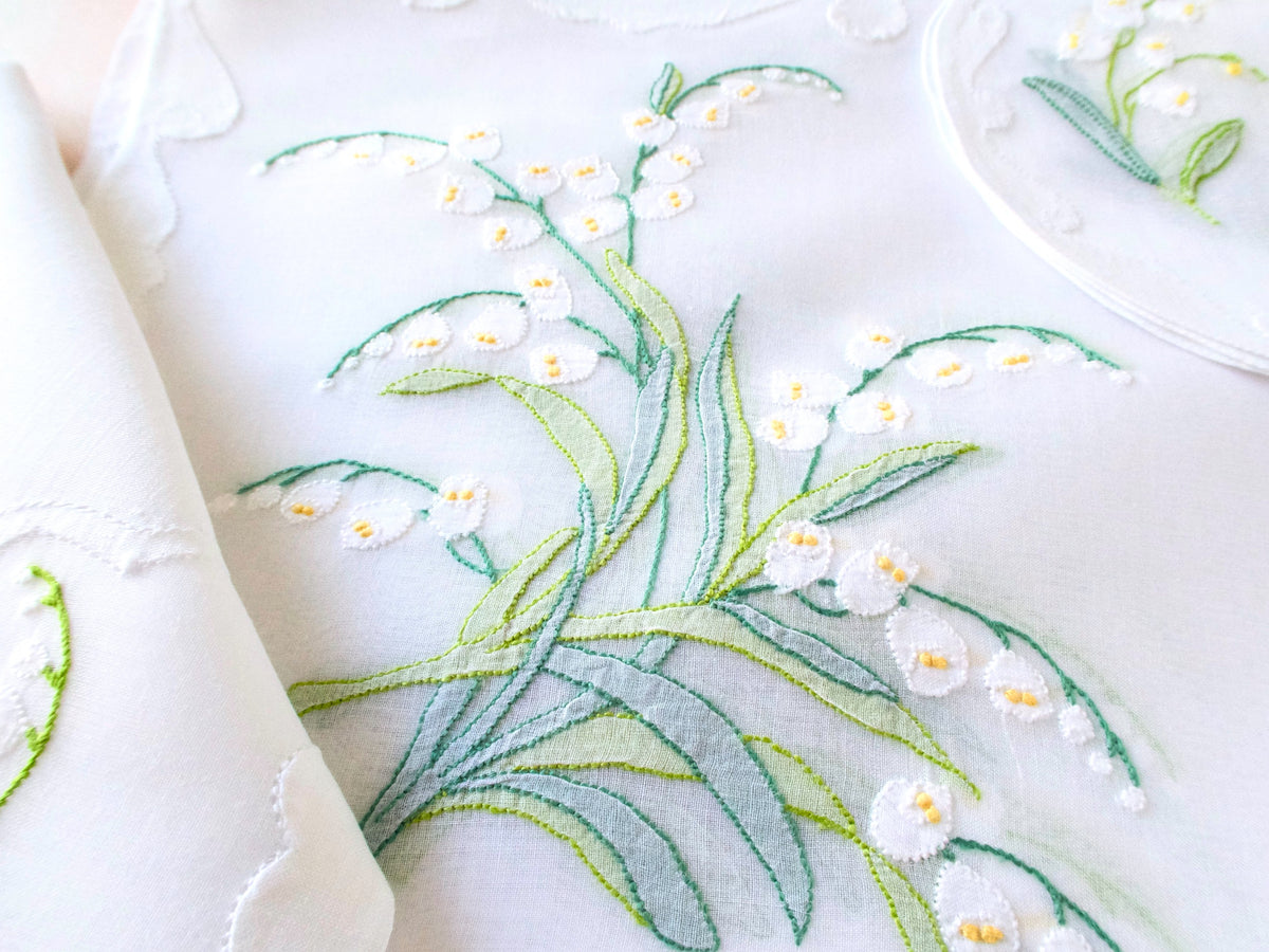 Close-up of hand embroidered Lily of the Valley on sheer organdy placemat, Madeira shadow work with white blossoms and yellow centers.