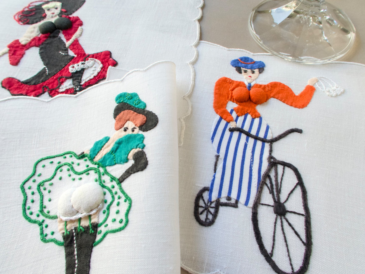 Close-up of vintage Madeira linen cocktail napkins by Paragon featuring playful hand-embroidered ladies with dimensional appliqué and bright colors.
