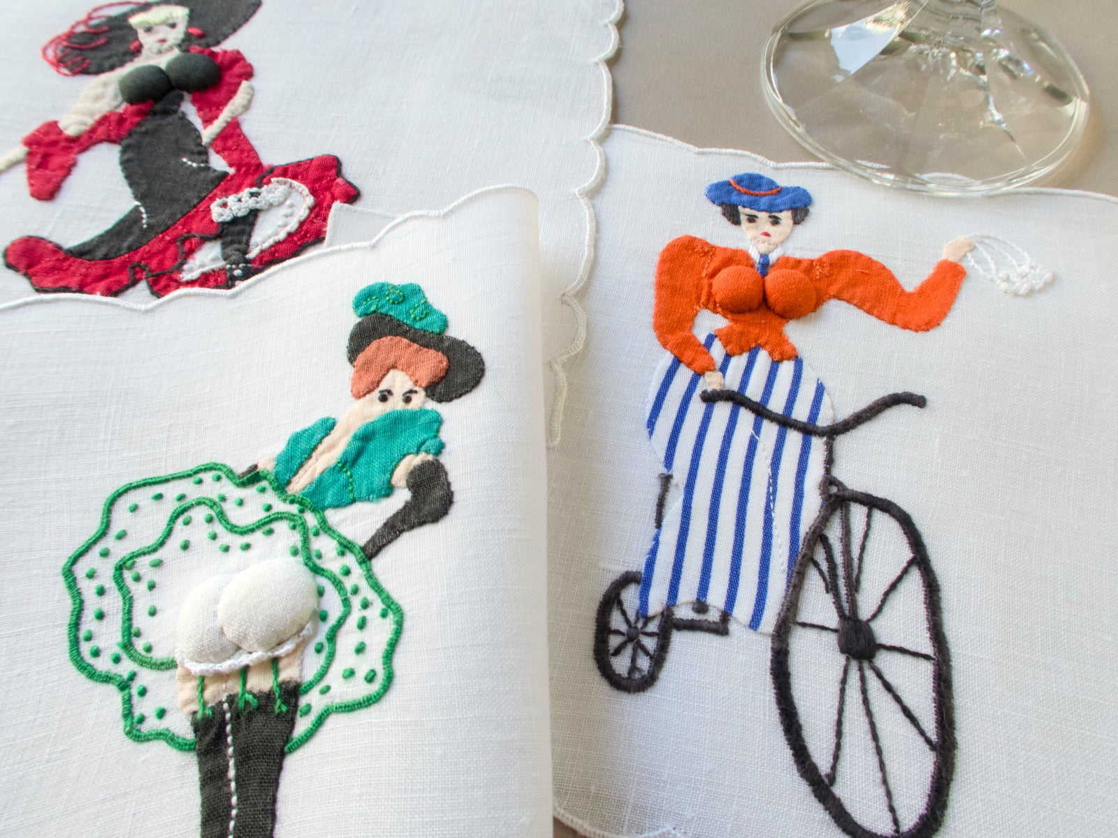 Close-up of vintage Madeira linen cocktail napkins by Paragon featuring playful hand-embroidered ladies with dimensional appliqué and bright colors.