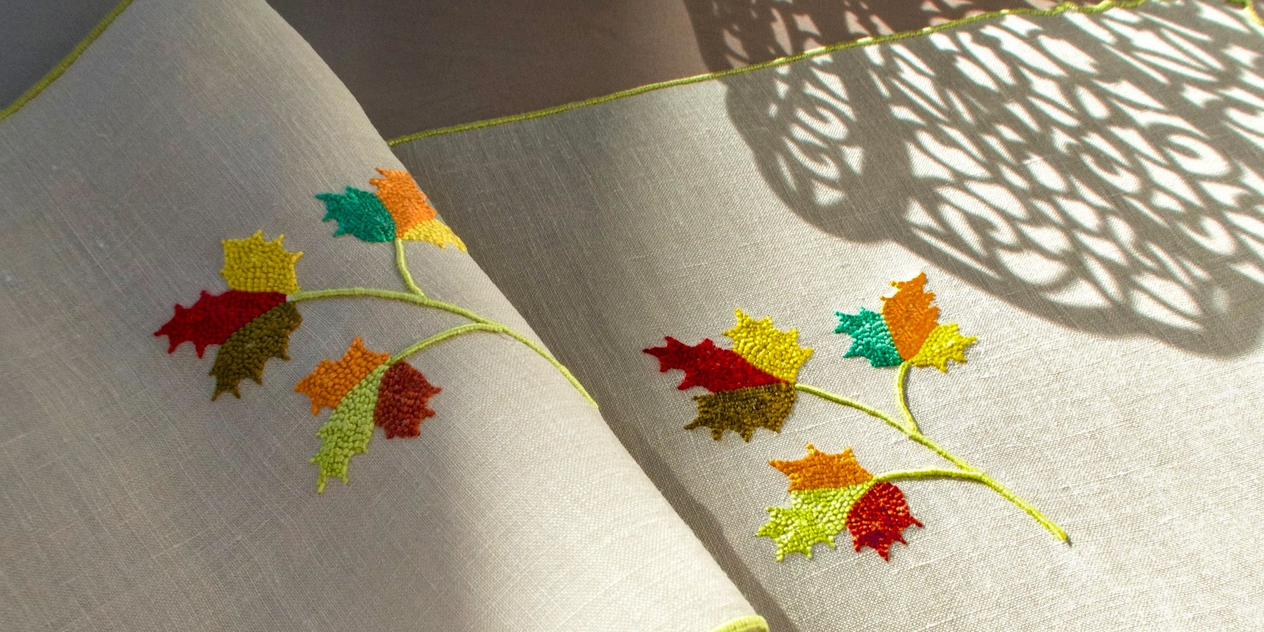 Vintage Marghab linen cocktail napkins with hand-embroidered maple leaves in autumn colors, shown in warm natural light and soft shadow.