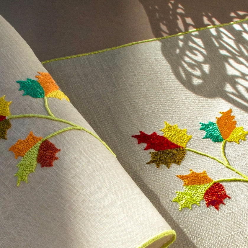 Vintage Marghab linen cocktail napkins with hand-embroidered maple leaves in autumn colors, shown in warm natural light and soft shadow.
