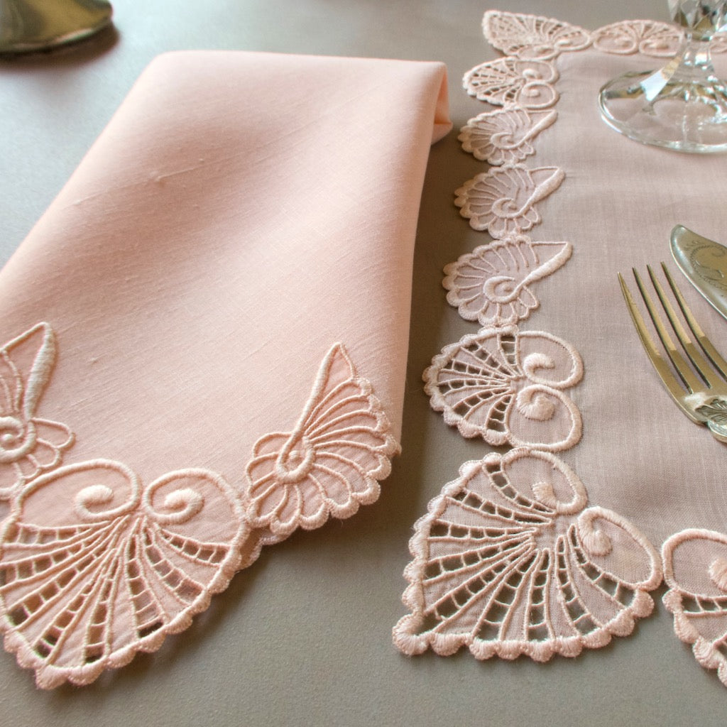 Vintage Marghab placemat and napkin set in soft blush linen, hand embroidered in Madeira with intricate shell motifs. Shown with silver flatware and glassware in natural light.