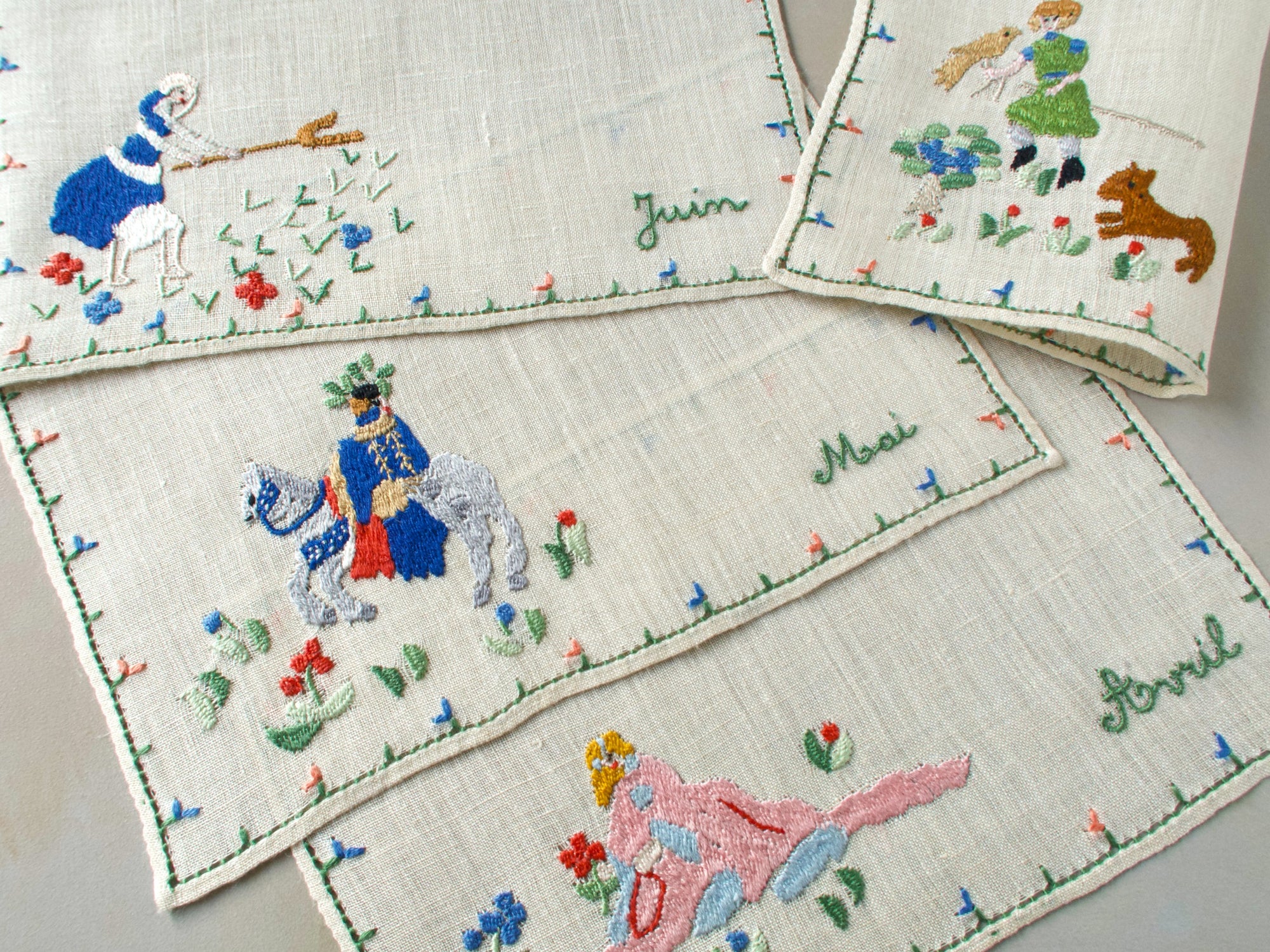 Close-up of several Rapisardi cocktail napkins showing figures for Avril, Juin, and Mai with small floral motifs.
