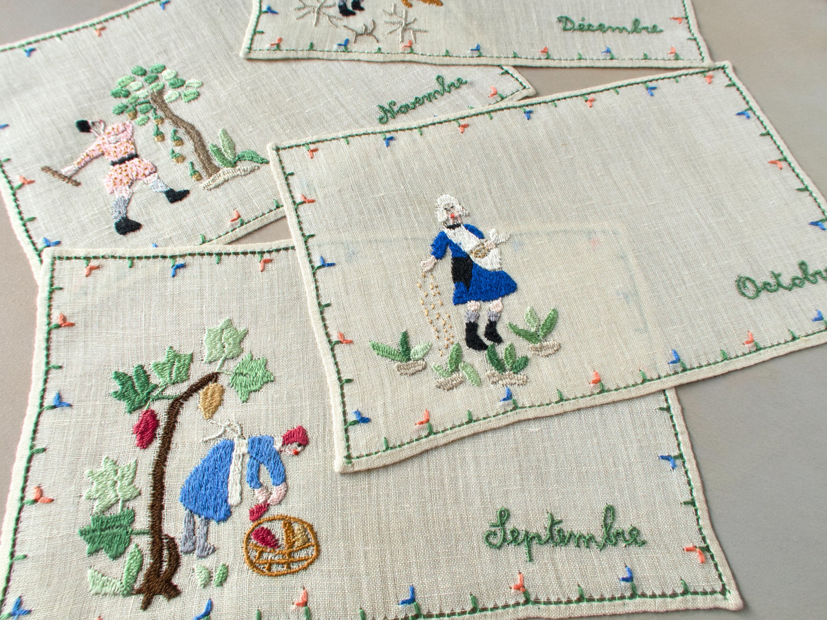 Cocktail napkins for September and October featuring embroidered figures in blue medieval dress with seasonal tasks