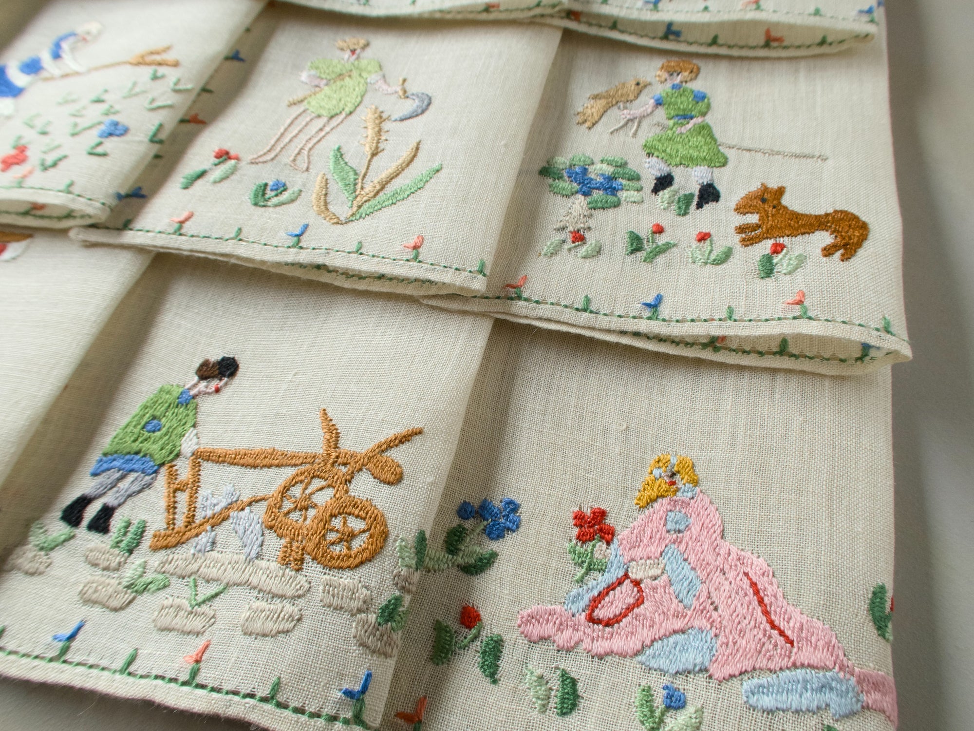Close-up showing June and July napkins with embroidered agricultural scenes including a plow and floral accents.