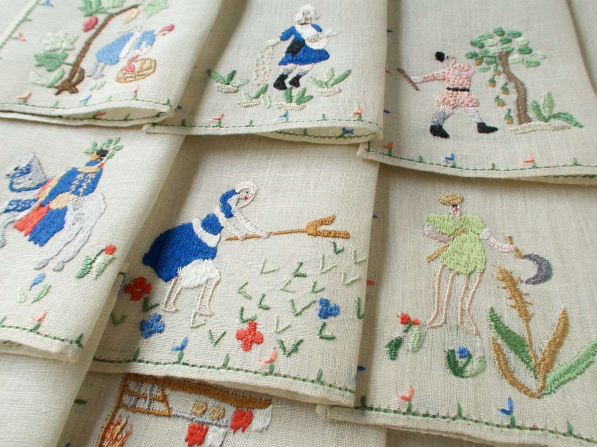 Close-up of three embroidered monthly scenes including August, September, and November, with figures in motion and scattered florals.