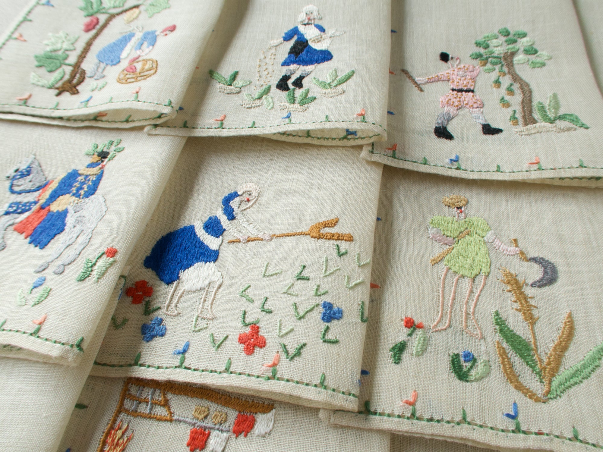 Close-up of three embroidered monthly scenes including August, September, and November, with figures in motion and scattered florals.