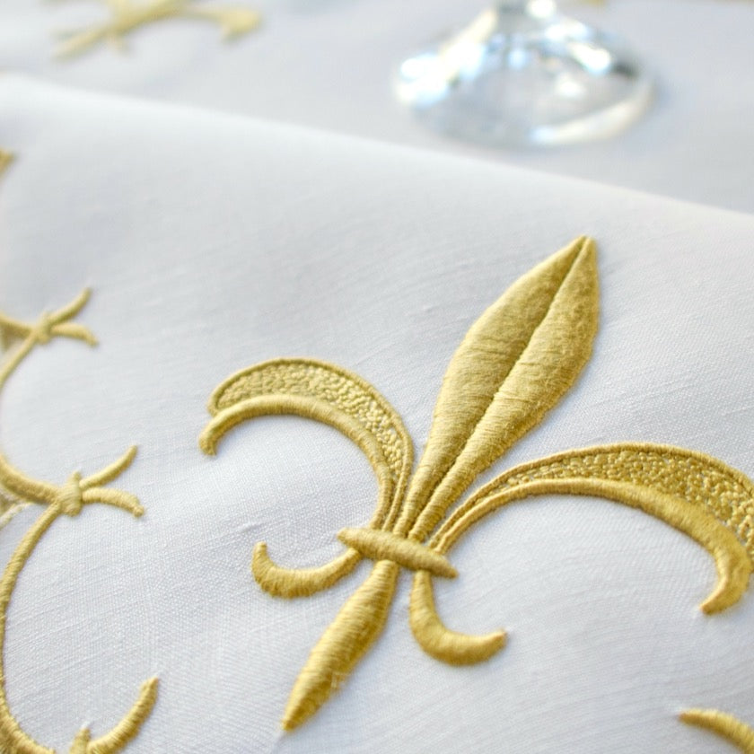 Vintage placemat featuring Marghab's gold fleur-de-lis pattern on white linen,  with a glass in the background