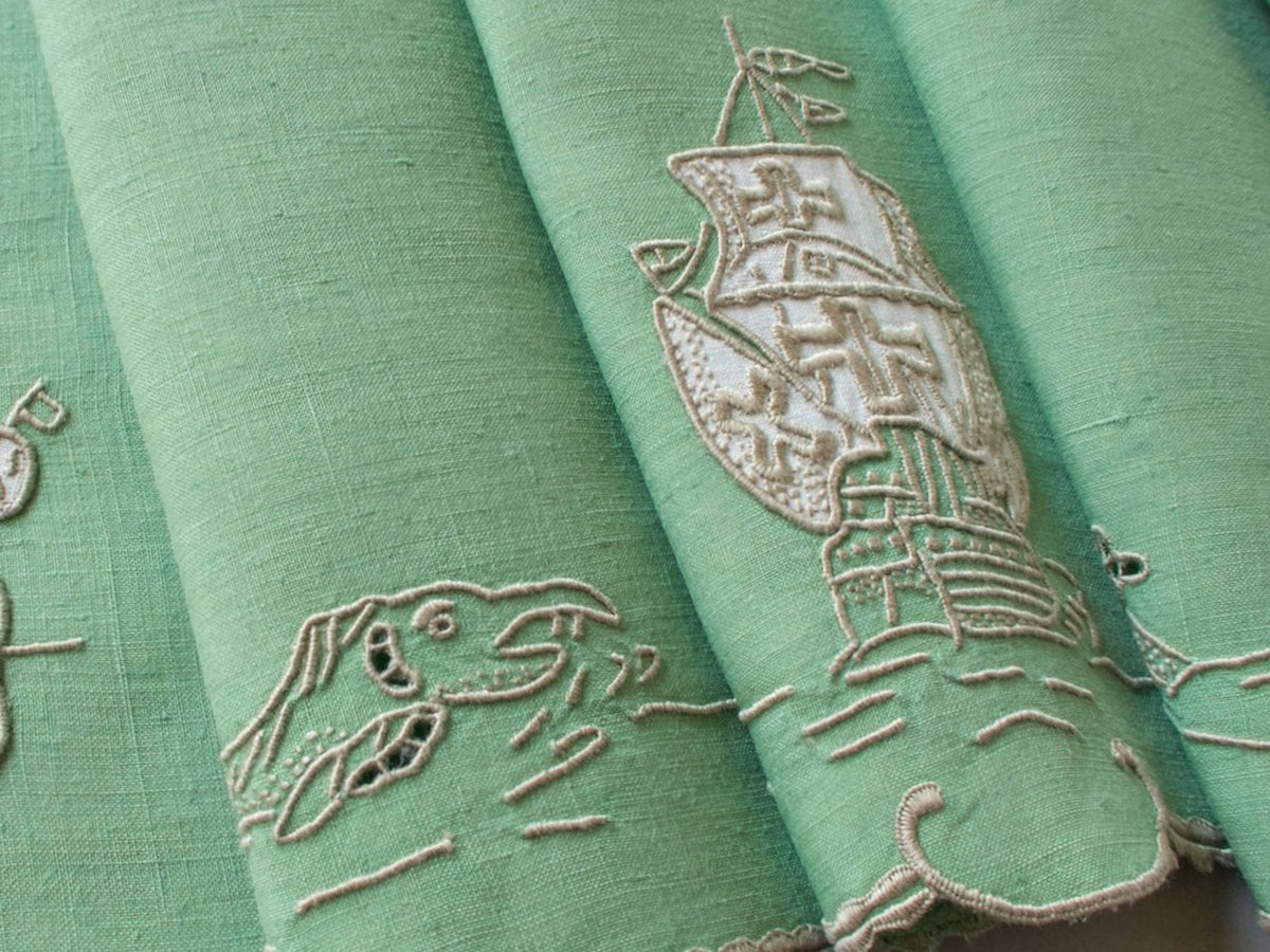 Vintage Marghab “Old Ships” placemat and napkin set, hand embroidered in Madeira on fine Irish linen in sea-green tones, featuring ships, waves, and mythical sea creatures in intricate raised embroidery.