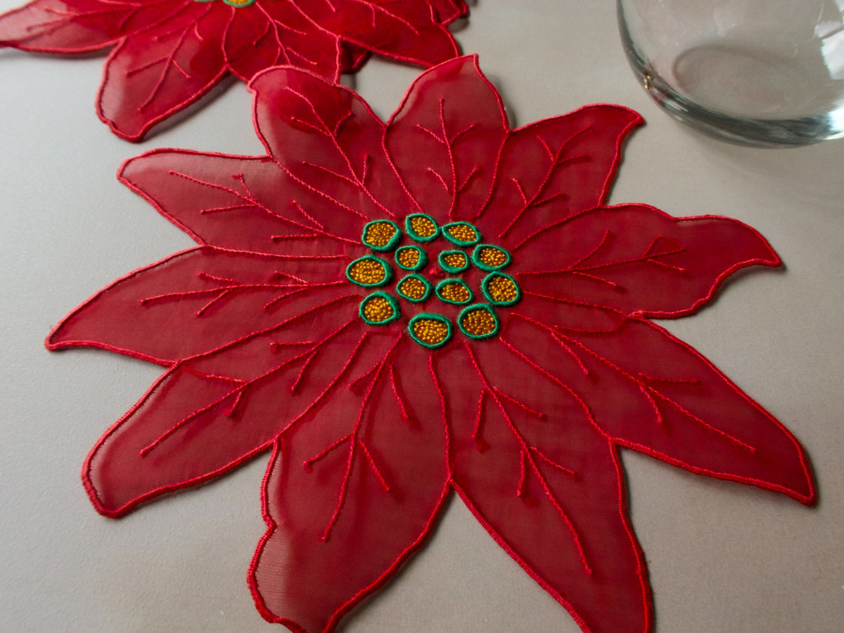 Red poinsettia-shaped organdy cocktail napkin with stitched petal outlines and green and gold embroidered center.