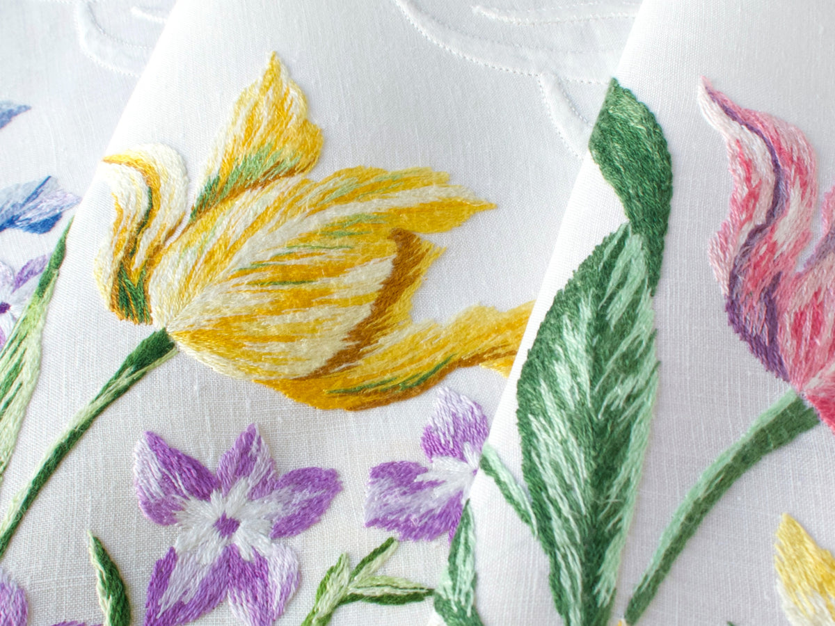 Macro detail of a single hand embroidered yellow tulip on vintage D. Porthault French linen, showing painterly thread shading.