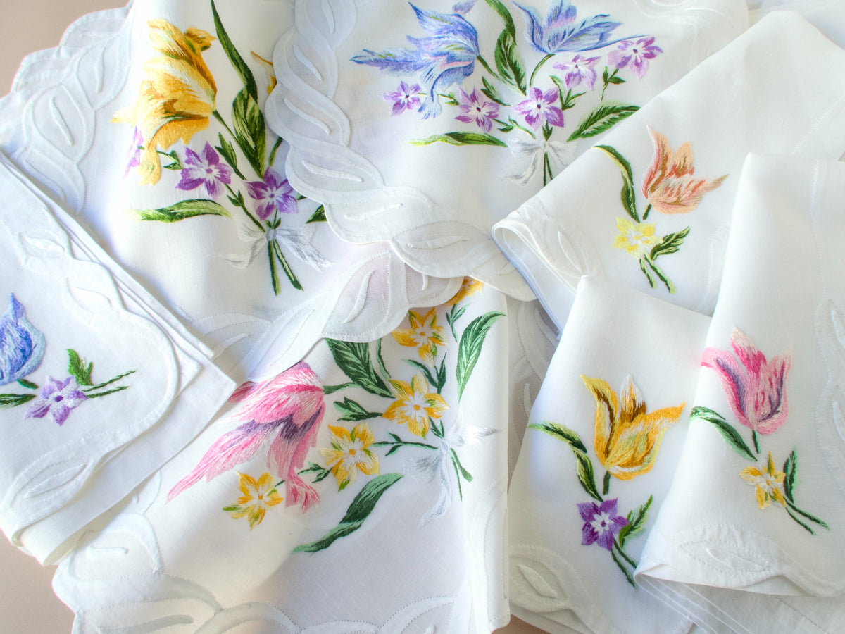 Multiple vintage D. Porthault French linen napkins arranged loosely, embroidered with multicolor tulips and wildflowers, shot under prismatic light.​​​​​​​​​​​​​​​​
