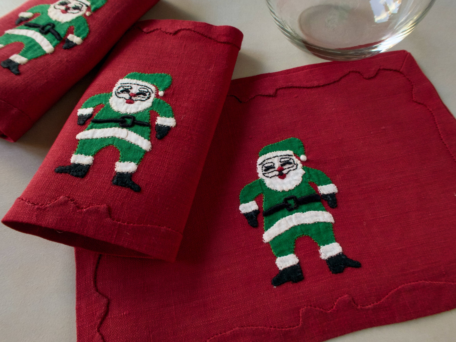 Red linen cocktail napkins with a hand-embroidered Santa in green suit, close-up, handmade in Madeira