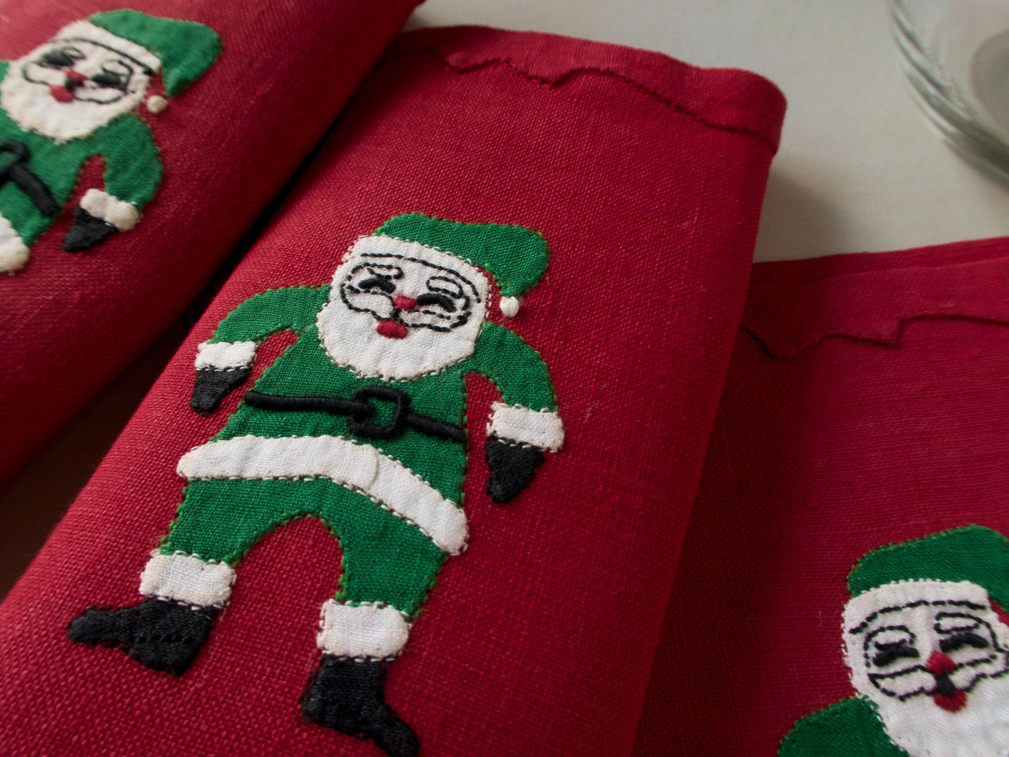 Red linen cocktail napkins with a hand-embroidered Santa in green suit, close-up, handmade in Madeira