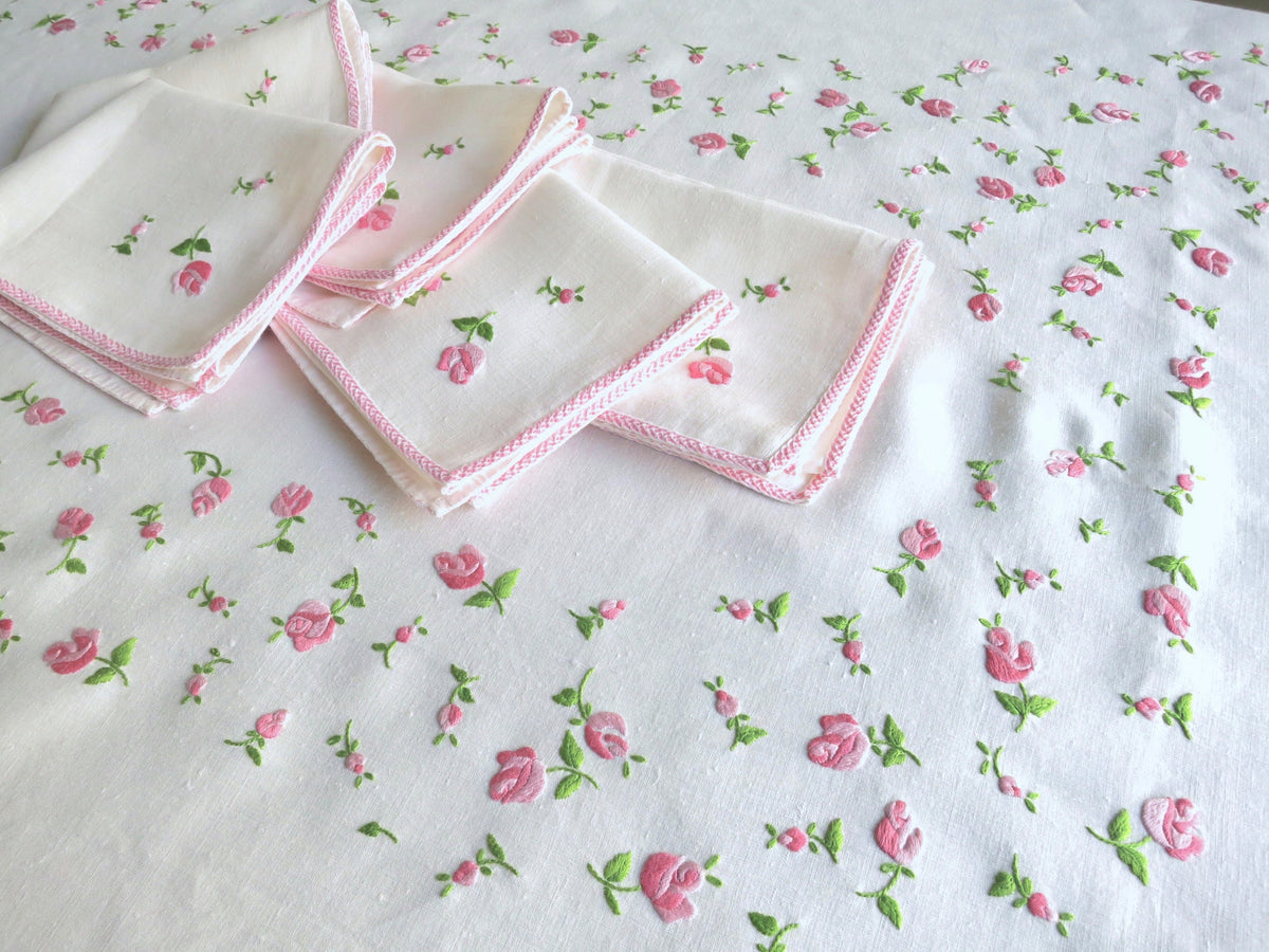 Detail of vintage European linen tablecloth showing pink embroidered border and scattered rosebud embroidery across white linen
