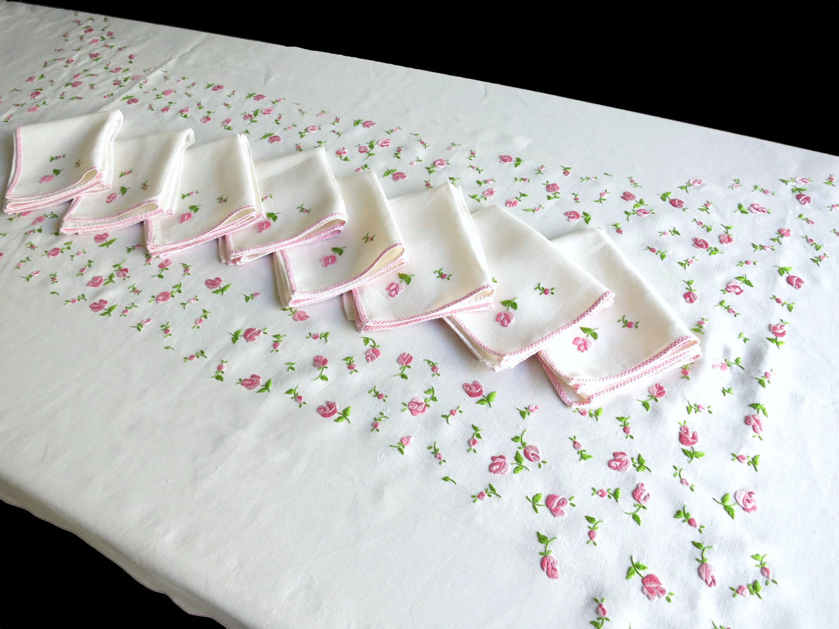 Full overhead view of vintage European linen tablecloth hand embroidered with scattered rosebuds across the entire cloth, with eight folded napkins displayed