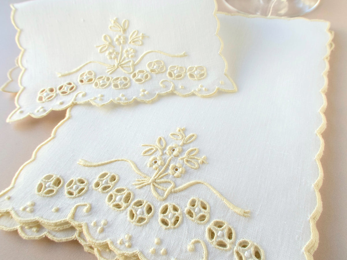 Vintage Madeira cocktail napkin showing ribbon bow and flower spray embroidery with dense cutwork eyelet border and scalloped edge.