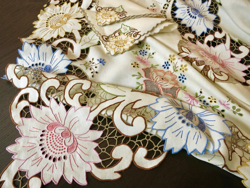 Close-up of colorful Madeira Richelieu embroidery with pink, yellow, and blue flowers on linen, highlighting fine needlework and openwork cutwork detail.